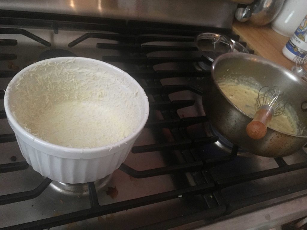 Preparing a soufflé dish with duck fat spray and finely grated cheese